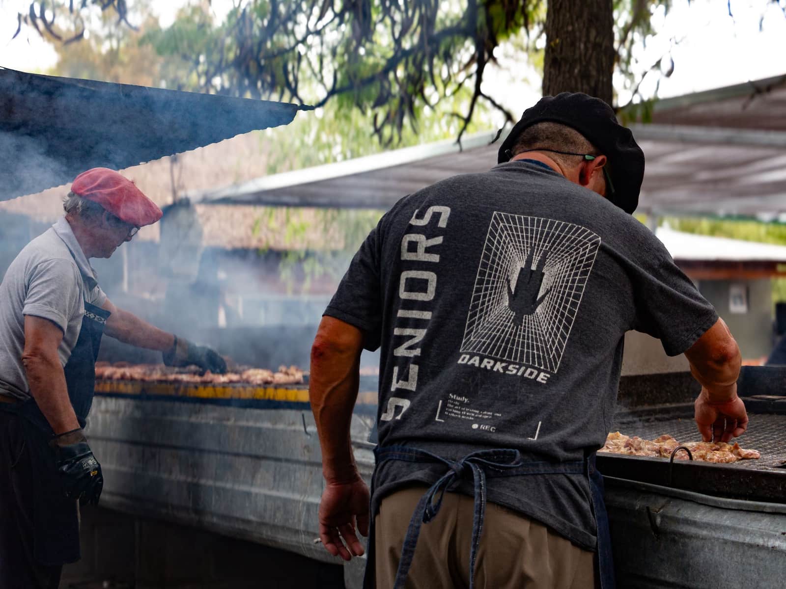 Two cooks working an outdoor barbecue grill, seen from behind