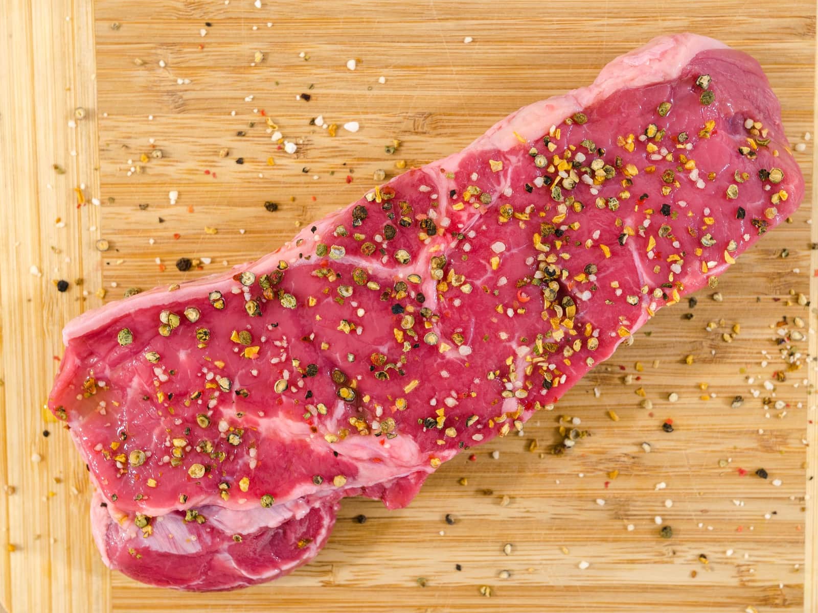 A raw steak cracked with pepper on a wooden board