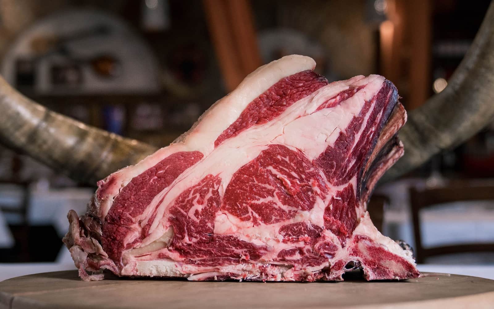 A thick bone-in rib roast, raw and well marbled, on a butcher's table