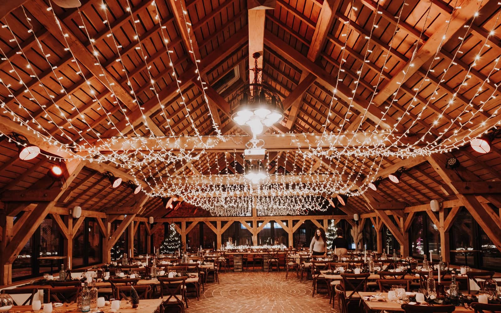 A timber barn strung with hundreds of lights over long dinner tables